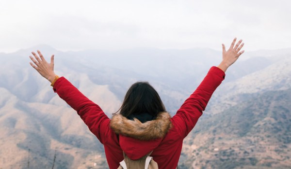 Woman reaching mountain peak, symbolizing success.